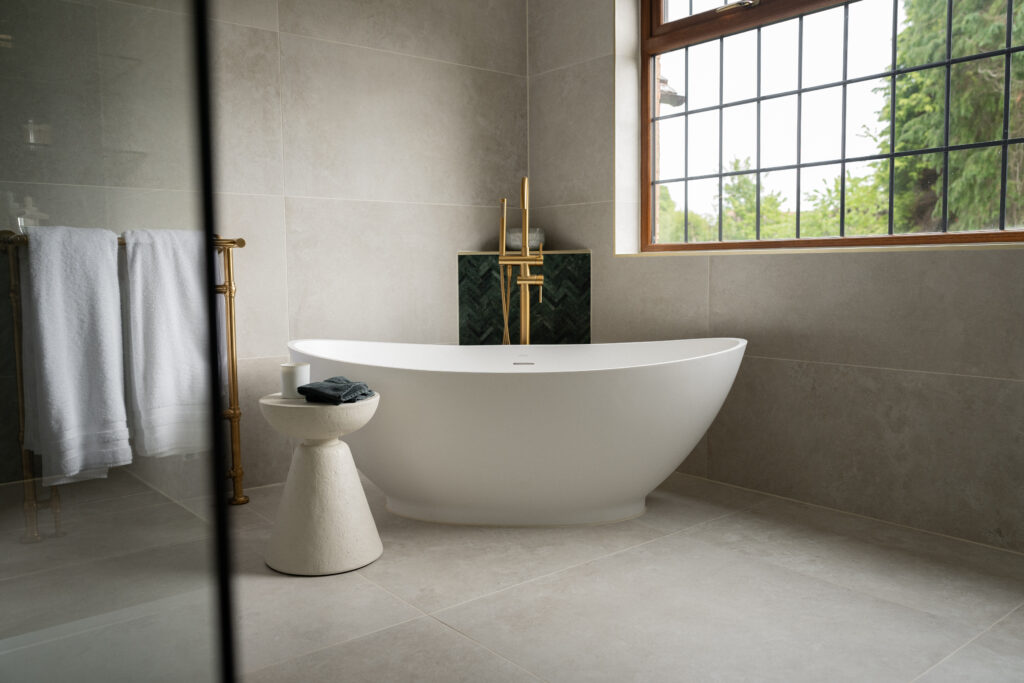 Freestanding bath and brushed brass fittings beneath a traditional multi-pane window in a renovated Alloway period home